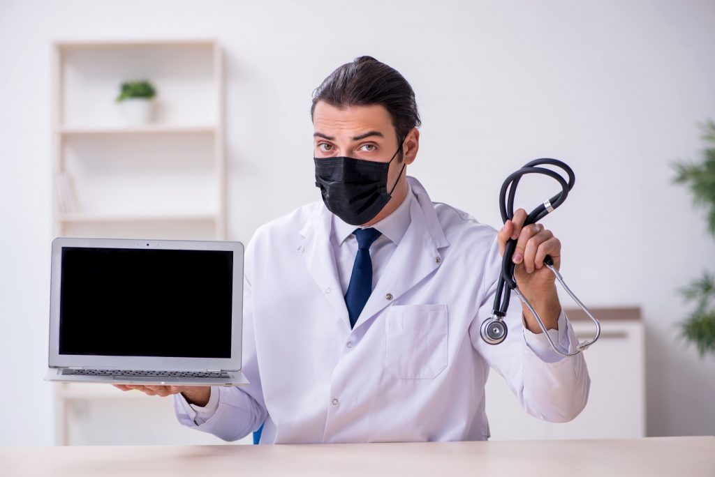Photo d'un medecin tenant dans sa main droite un ordinateur portable et dans la gauche un stéthoscope obstétrical