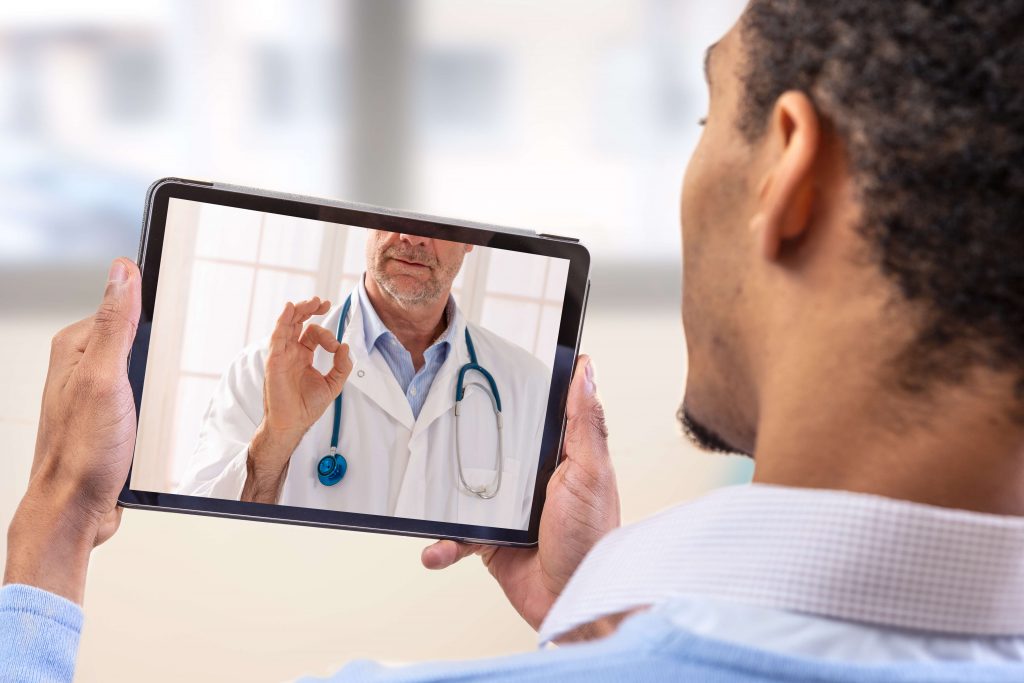 Un homme parlant a son médecin en vidéo avec une tablette dans les mains.